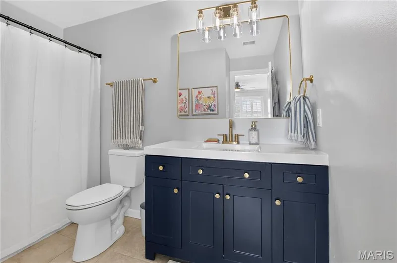 Bathroom featuring a navy blue vanity with gold-tone hardware, a white countertop, an undermount sink, and a gold-framed mirror — 302 Oak Stand Court, Chesterfield, MO 63005