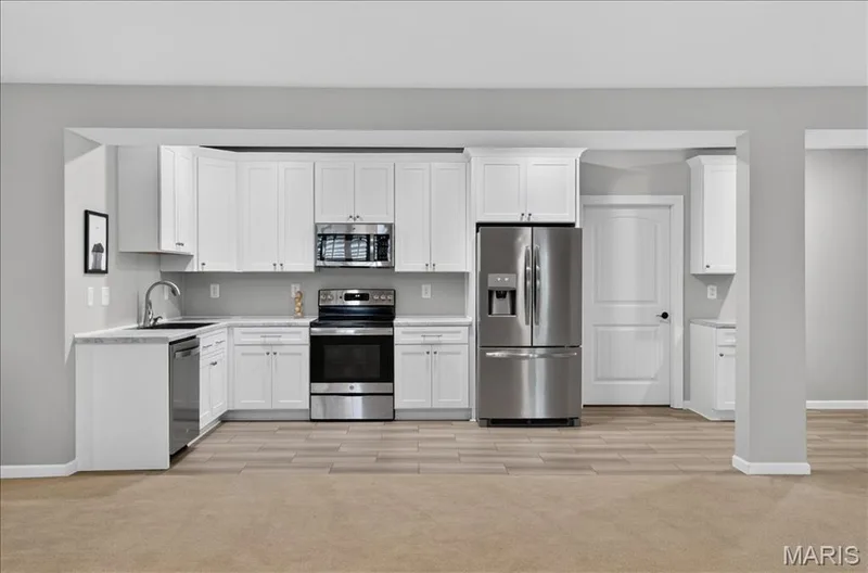 Open-concept kitchen featuring white shaker cabinetry, stainless steel appliances, light-toned countertops, and wood-finish flooring — 302 Oak Stand Court, Chesterfield, MO 63005