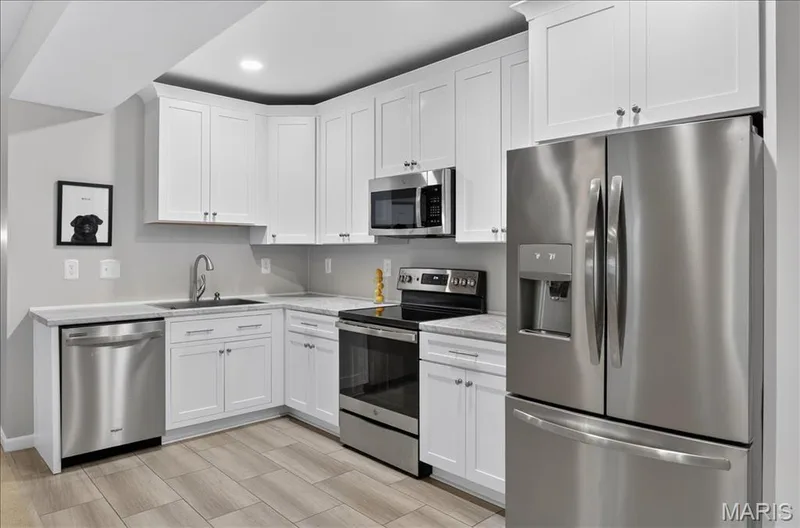 Kitchen featuring white shaker-style cabinetry, light-toned countertops, and stainless steel appliances including a French door refrigerator, built-in microwave, range, and dishwasher — 302 Oak Stand Court, Chesterfield, MO 63005