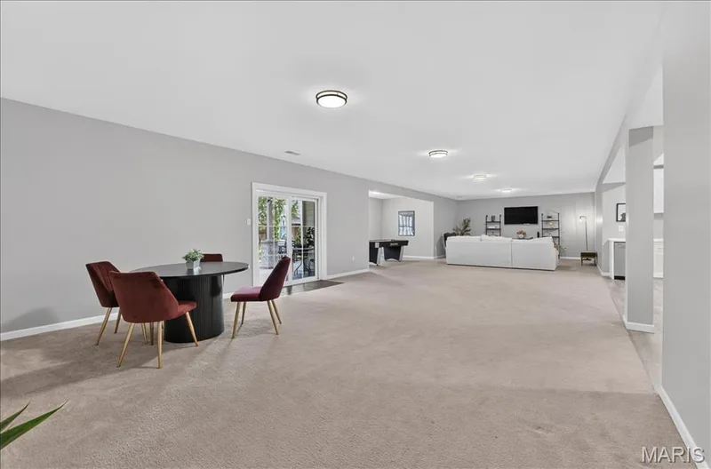 Expansive recreation room featuring light gray walls, plush carpeting, recessed lighting, and a white sliding glass door providing outdoor access — 302 Oak Stand Court, Chesterfield, MO 63005