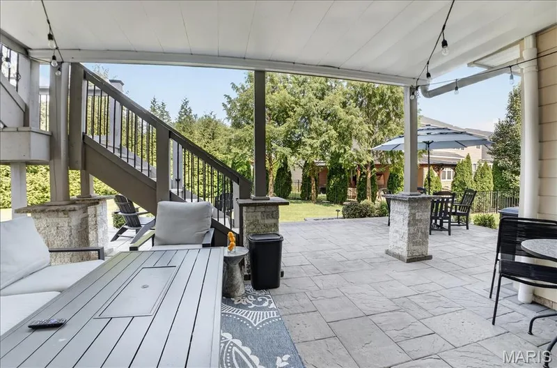 Covered outdoor patio featuring stone-look pavers, a built-in fire table, and string lighting — 302 Oak Stand Court, Chesterfield, MO 63005
