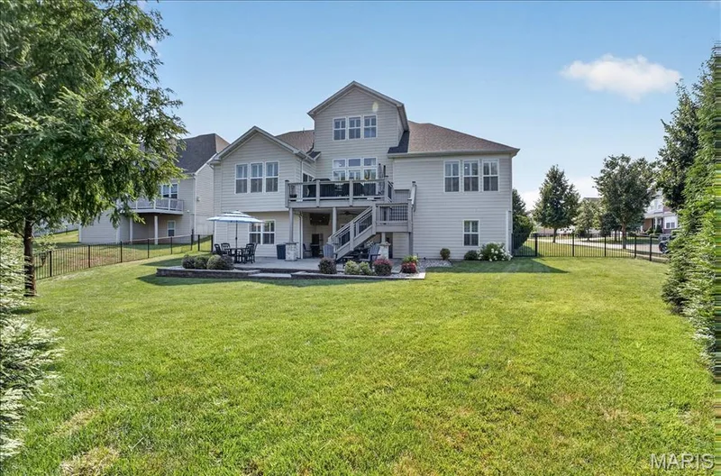 Expansive backyard featuring a manicured lawn, a two-story residence with light-colored siding, multiple windows, a second-story deck, and a ground-level patio — 302 Oak Stand Court, Chesterfield, MO 63005