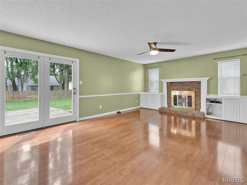 Family room with wood burning fireplace, built ins, wood flooring, and doors leading to the large, level backyard. — 34 Shadow Creek Drive, St Peters, MO 63376
