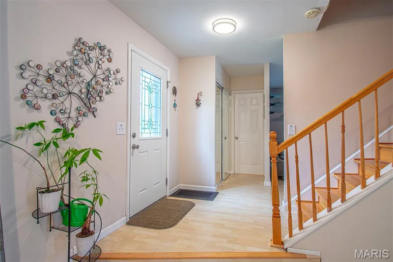 MAIN ENTRANCE - Entrance Foyer with mirror door Coat Closet. Entryway featuring a white door with decorative glass inserts, wood-finish flooring, a wood staircase, and mirrored closet doors. — 13261 COCHERO Drive, Chesterfield, MO 63141