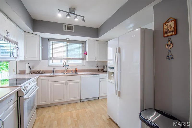 KITCHEN - Bright kitchen featuring white cabinetry, light wood-finish flooring, a window with blinds, a built-in microwave, and track lighting — 13261 COCHERO Drive, Chesterfield, MO 63141