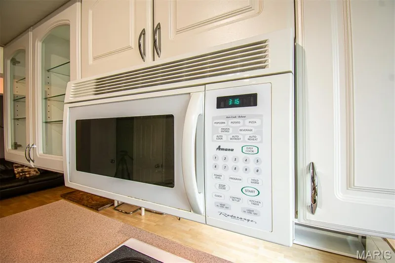 KITCHEN - Kitchen featuring white cabinetry, an over-the-range microwave, glass-front display cabinets, and a light-toned countertop — 13261 COCHERO Drive, Chesterfield, MO 63141
