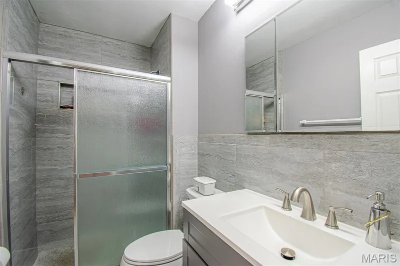 PRIMARY BATHROOM – Beautifully Remodeled & featuring a glass-enclosed shower with tile surround, a built-in shower niche, a dark gray vanity with an integrated sink, a brushed nickel faucet, and a wall-mounted medicine cabinet with mirrored doors — 13261 COCHERO Drive, Chesterfield, MO 63141