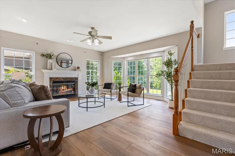 Welcoming living room with an open-concept layout, elegant staircase, gas fireplace, and large bay window wall offering so much natural light. — 354 Buckington Street, St Peters, MO 63376
