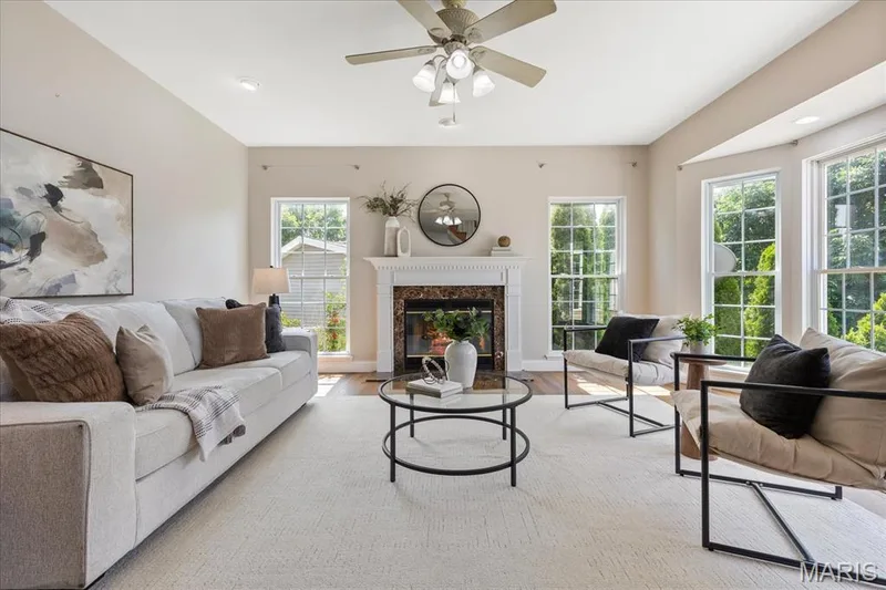 Light-filled living room featuring a cozy gas fireplace, brand-new luxury vinyl plank flooring, and expansive bay window wall offering serene outdoor views. — 354 Buckington Street, St Peters, MO 63376