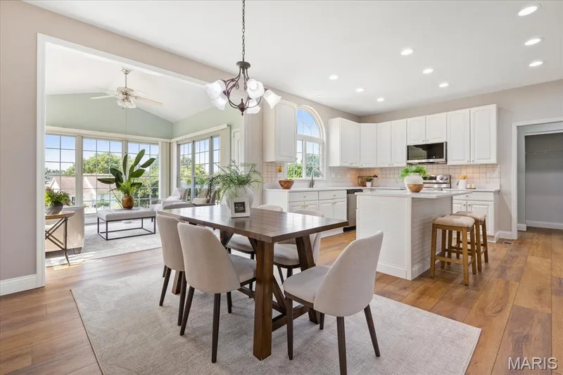 Bright, open kitchen and breakfast room with modern white cabinetry, central island with breakfast bar, and adjacent light-filled sunroom. Morning coffee easily leads to weekend gatherings in this bright, seamless kitchen-to-sunroom space. — 354 Buckington Street, St Peters, MO 63376
