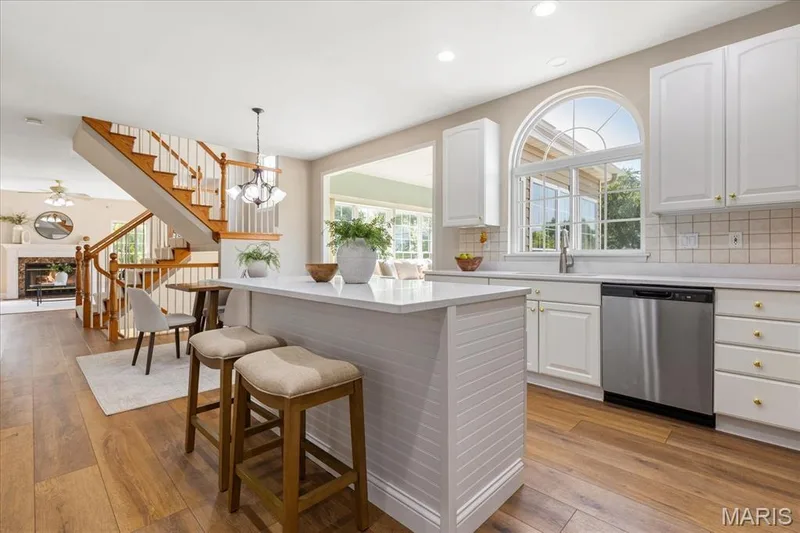 Light pours through the arched kitchen window, illuminating the beadboard center island and warm luxury vinyl plank flooring. — 354 Buckington Street, St Peters, MO 63376