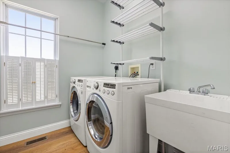 Main-level laundry room fitted with front-load washer/dryer units, utility sink, drying rack system, and natural lighting. — 354 Buckington Street, St Peters, MO 63376