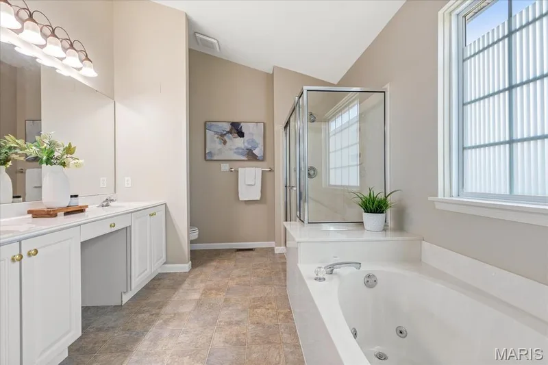 Primary ensuite bathroom boasting a dual-sink vanity, corner soaking tub, and separate glass-enclosed shower with seat. — 354 Buckington Street, St Peters, MO 63376