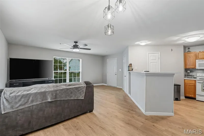 Open-concept living area featuring wood-finish flooring, a contemporary ceiling fan, and a kitchen with warm-toned cabinetry — 640 Homerun Drive #37N, O'Fallon, MO 63366