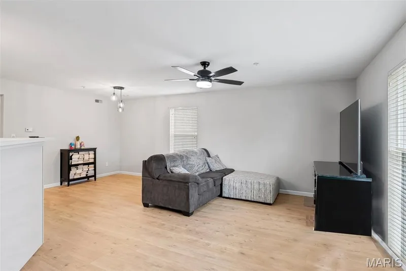 Open-concept living space featuring light wood-finish flooring, a ceiling fan with integrated lighting, and a modern pendant light fixture — 640 Homerun Drive #37N, O'Fallon, MO 63366
