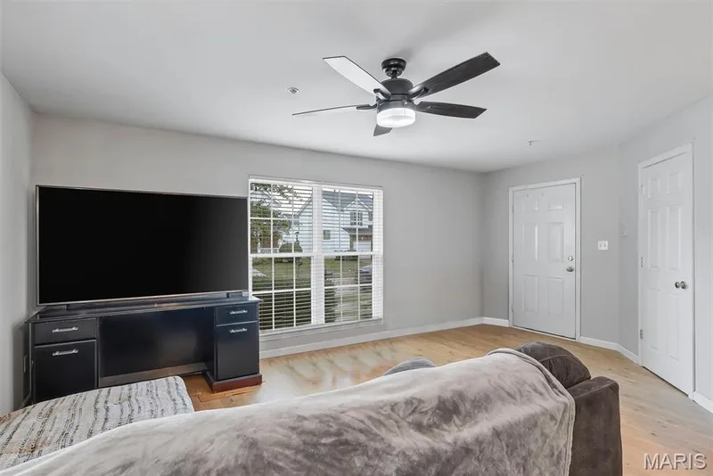 Bright living area featuring wood-finish flooring, a contemporary ceiling fan with integrated lighting, and a white paneled entry door — 640 Homerun Drive #37N, O'Fallon, MO 63366