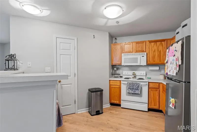 Kitchen featuring wood-finish cabinetry, light-toned countertops, and a full suite of white and stainless steel appliances — 640 Homerun Drive #37N, O'Fallon, MO 63366