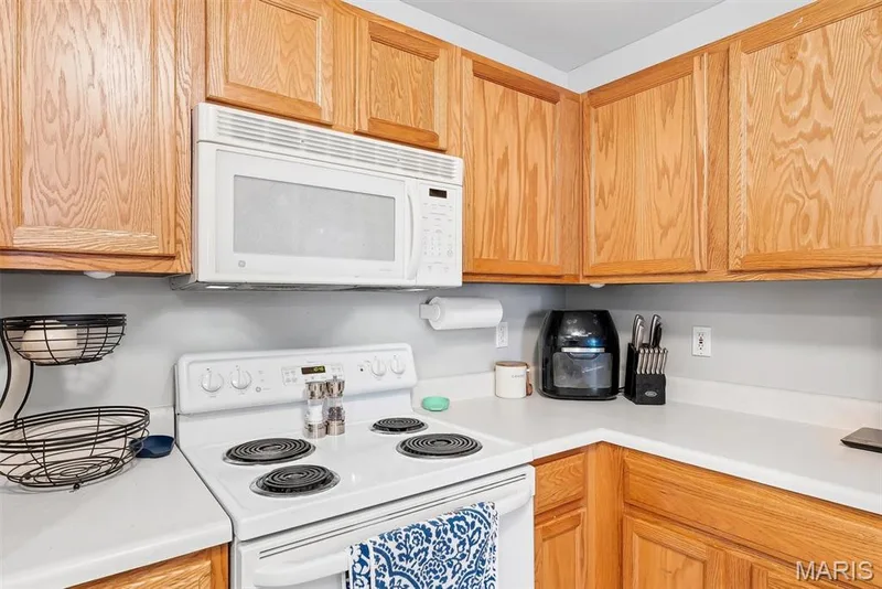 Kitchen featuring light wood-finish cabinetry, white countertops, a white electric range, and an over-the-range microwave — 640 Homerun Drive #37N, O'Fallon, MO 63366