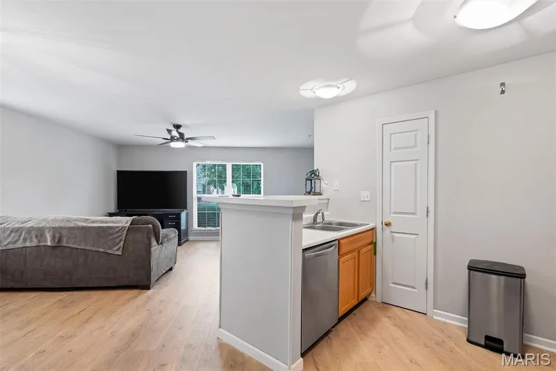 Open-concept living space featuring wood-finish flooring, a kitchen peninsula with a stainless steel sink and dishwasher, light wood cabinetry, and a ceiling fan with integrated lighting — 640 Homerun Drive #37N, O'Fallon, MO 63366