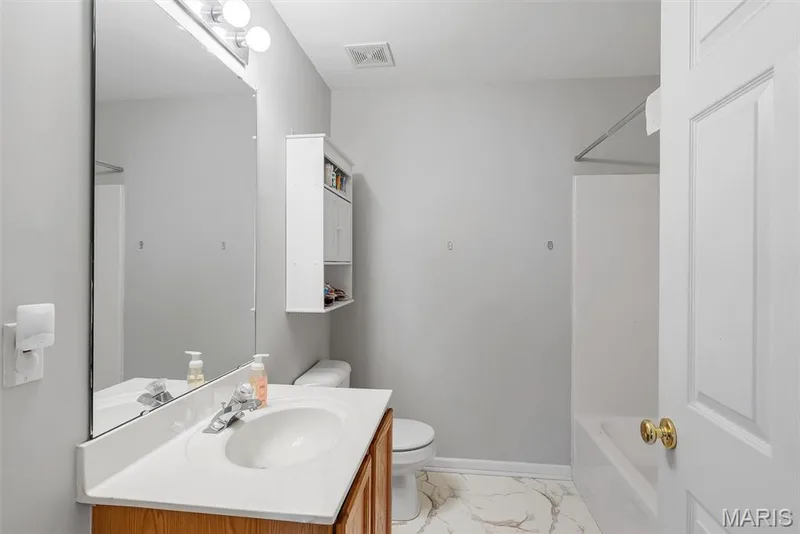 Bathroom featuring a white bathtub, wood-finish vanity with an integrated sink, wall-mounted mirror, overhead lighting, and built-in wall cabinet — 640 Homerun Drive #37N, O'Fallon, MO 63366