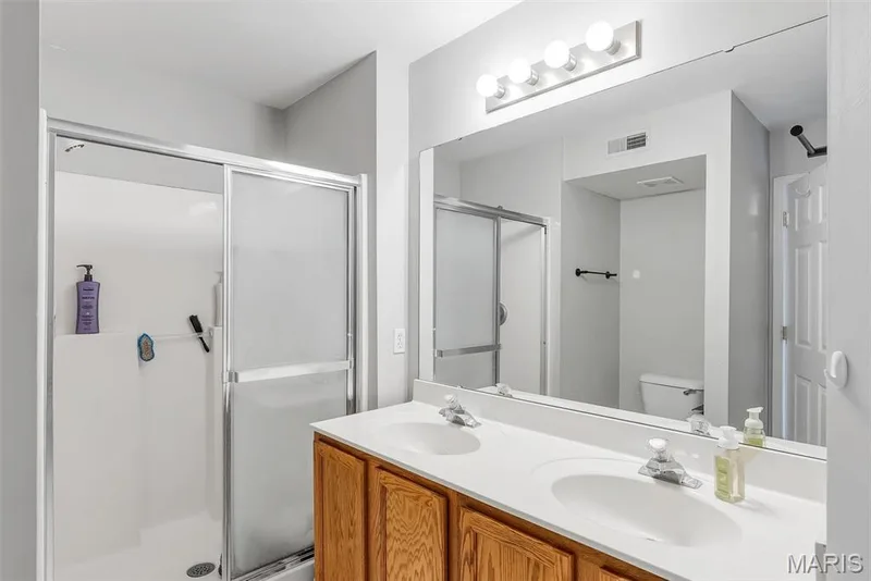 Bathroom featuring a dual vanity with white countertops, wood-finish cabinetry, and a full-width mirror — 640 Homerun Drive #37N, O'Fallon, MO 63366