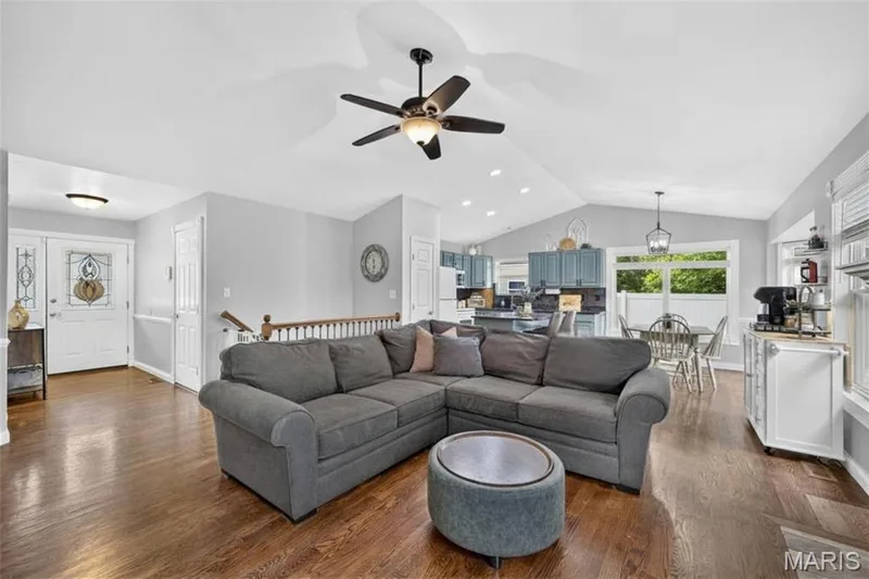 Vaulted ceiling with a ceiling fan and recessed lighting, wood-finish flooring, white paneled entry door with decorative glass sidelights, and a kitchen featuring blue cabinetry — 708 Woodland Ridge Drive, St Peters, MO 63376
