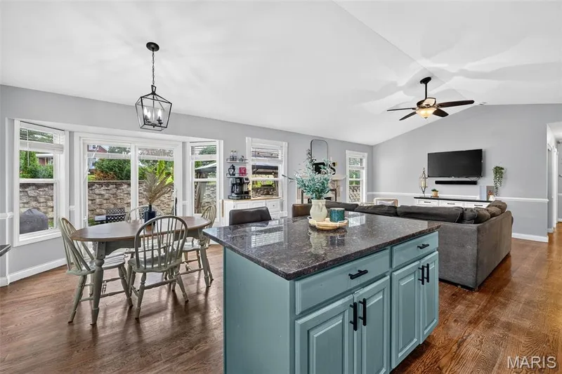 Open-concept layout featuring wood-finish flooring, a kitchen island with stone countertop, and a dining area with bay windows — 708 Woodland Ridge Drive, St Peters, MO 63376