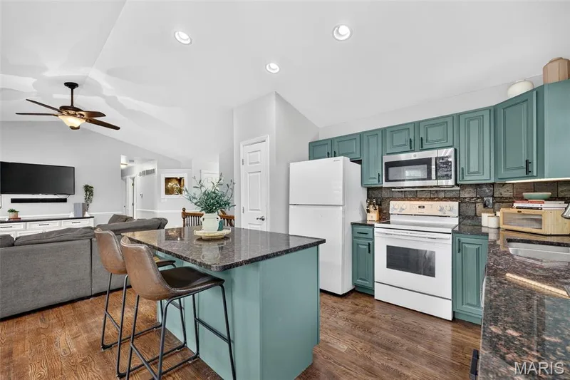 Kitchen with wood-finish flooring, granite countertops, teal cabinetry, and stainless steel microwave — 708 Woodland Ridge Drive, St Peters, MO 63376