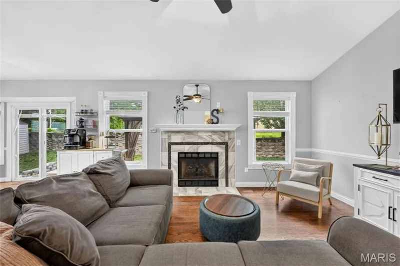 Wood-finish flooring, a fireplace with a stone surround and mantel, a ceiling fan, white base cabinetry with a countertop, and sliding glass doors — 708 Woodland Ridge Drive, St Peters, MO 63376