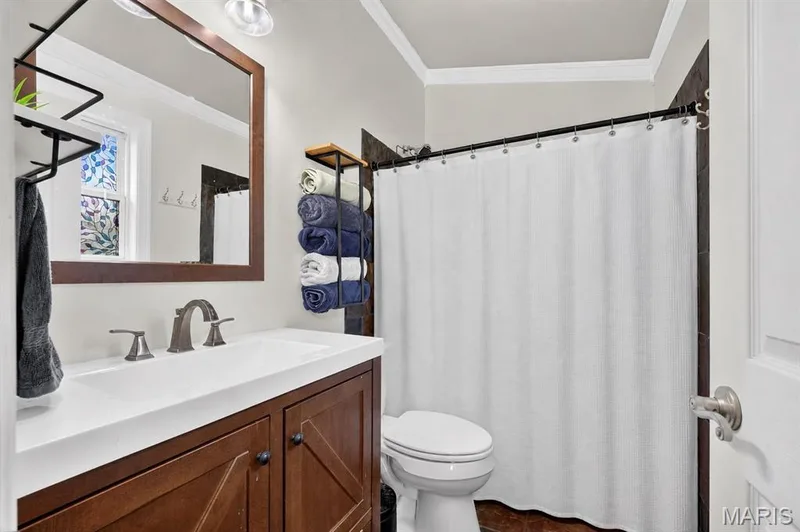 Wood-finish vanity with an integrated white sink, brushed nickel faucet, framed mirror, and crown molding — 708 Woodland Ridge Drive, St Peters, MO 63376