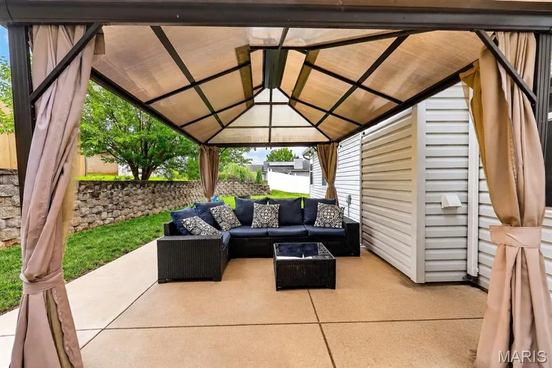 Covered patio featuring a solid-surface floor, stone retaining wall, and exterior siding — 708 Woodland Ridge Drive, St Peters, MO 63376