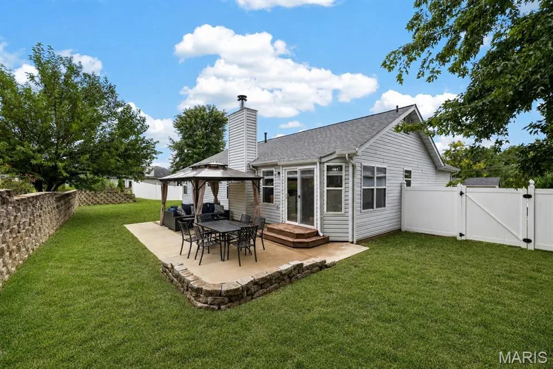 Expansive lawn with a concrete patio, stone retaining walls, and a white privacy fence — 708 Woodland Ridge Drive, St Peters, MO 63376