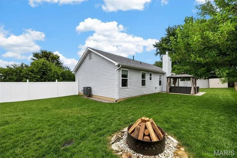 Expansive backyard featuring a white privacy fence, an integrated fire pit, and a covered patio structure — 708 Woodland Ridge Drive, St Peters, MO 63376