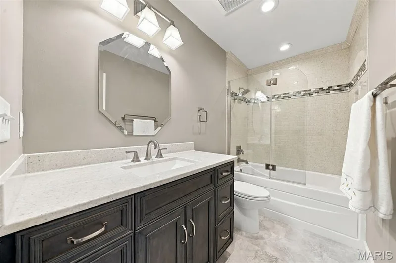 Hall bath has been updated with comfort height vanity, toilet, lighting, flooring and tile surround, glass door on tub/shower combo — 1230 Luray Drive, Chesterfield, MO 63017
