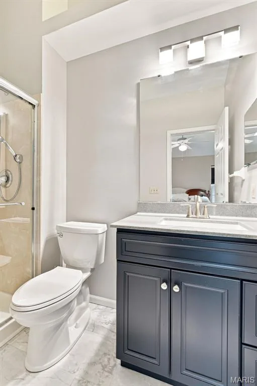 Shower enclosure with clear glass panel, vanity with dark blue cabinetry, light-toned countertop with integrated sink, wall-mounted mirror, and contemporary light fixture — 16561 Carriage View Court, Wildwood, MO 63040