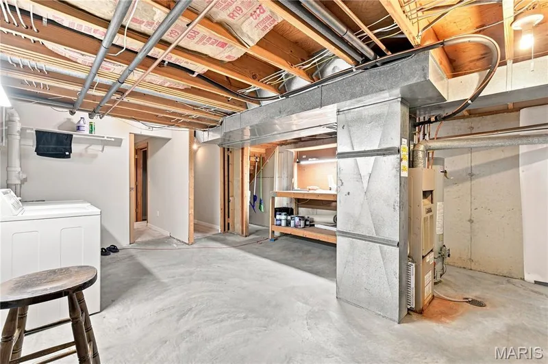 Finished basement featuring polished concrete flooring, exposed wood-beam ceiling with recessed lighting, and multiple utility zones including a wet bar with marble-finish countertop, built-in shelving, and a sauna enclosure — 16561 Carriage View Court, Wildwood, MO 63040