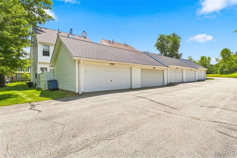 Multiple attached single-car garages with white overhead doors, exterior wall-mounted lighting, and a paved parking surface — 16561 Carriage View Court, Wildwood, MO 63040