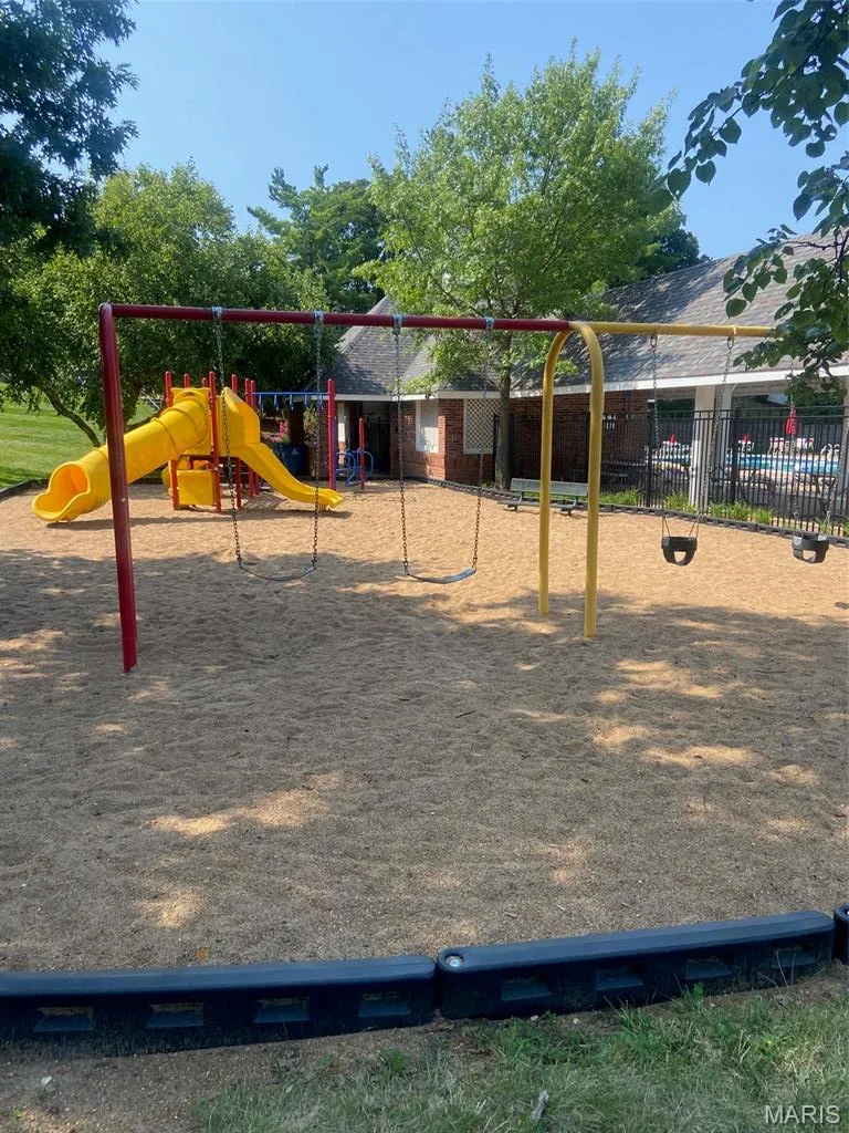 Recreational yard featuring multiple play structures including a yellow slide, swing set, and monkey bars, all situated on a sand surface — 16561 Carriage View Court, Wildwood, MO 63040