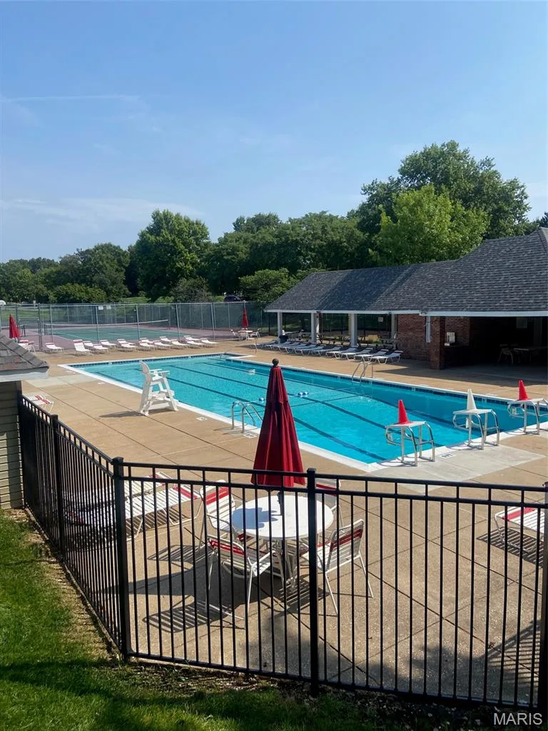 Community outdoor swimming pool with a surrounding concrete deck, enclosed by a black metal fence, and a nearby tennis court — 16561 Carriage View Court, Wildwood, MO 63040