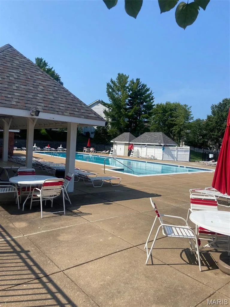 Paved patio area, two swimming pools, covered pavilion with shingle roof, white privacy fencing, and surrounding mature trees — 16561 Carriage View Court, Wildwood, MO 63040