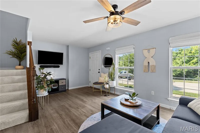 Living area featuring wood-finish flooring, light gray wall paint, and a ceiling fan with integrated lighting — 349 Shady Rock Lane, O'Fallon, MO 63368