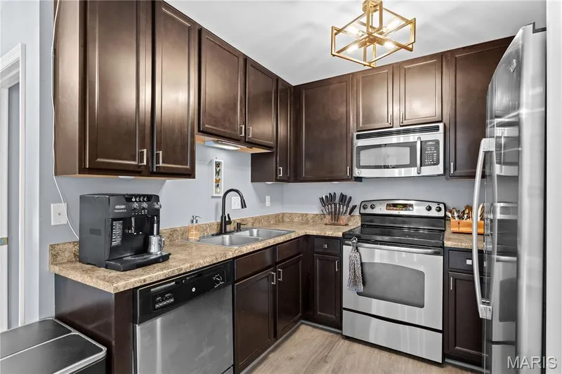 Kitchen featuring dark wood-finish cabinetry, stainless steel appliances, a double basin sink with a high-arch faucet, laminate countertops, and wood-finish flooring — 349 Shady Rock Lane, O'Fallon, MO 63368