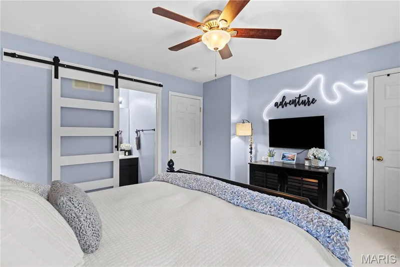 Spacious room featuring a white barn door with opaque glass panels, a ceiling fan with integrated lighting, and a separate white door — 349 Shady Rock Lane, O'Fallon, MO 63368