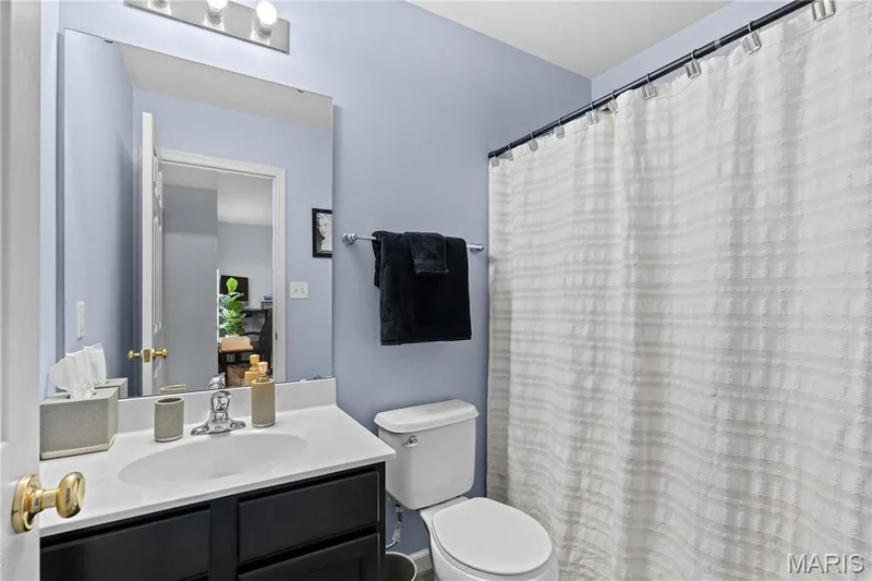 Bathroom featuring a vanity with a white countertop and dark base cabinetry, a wall-mounted mirror, and a full shower with a white curtain — 349 Shady Rock Lane, O'Fallon, MO 63368