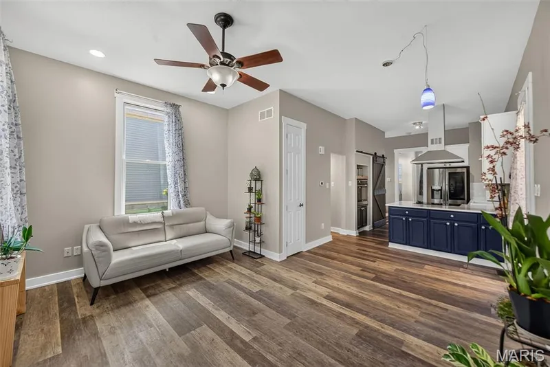 Open-concept living area featuring wood-finish flooring throughout, a ceiling fan with integrated lighting, and abundant natural light from large windows — 3471 Hiram Street, St Charles, MO 63301