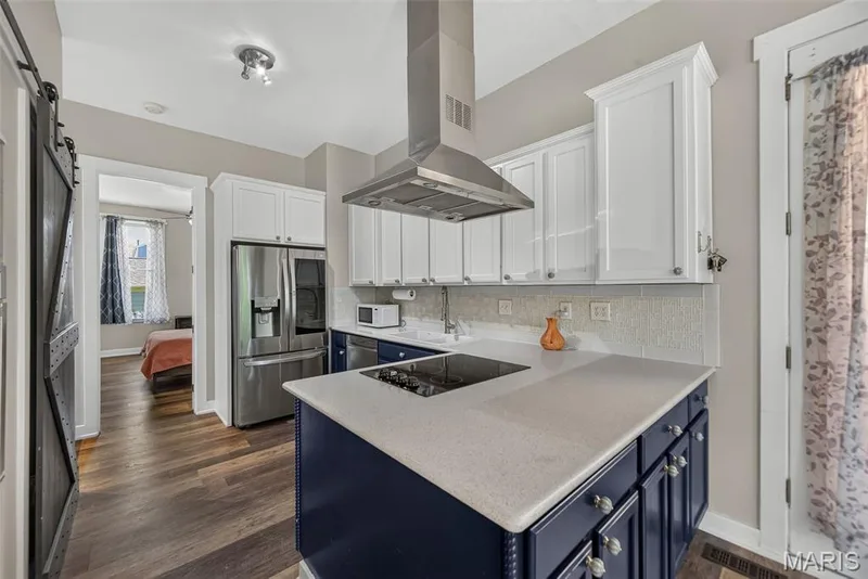 Modern kitchen featuring white shaker cabinetry, a stainless steel range hood, and a striking navy blue island with a light gray quartz countertop and built-in cooktop — 3471 Hiram Street, St Charles, MO 63301