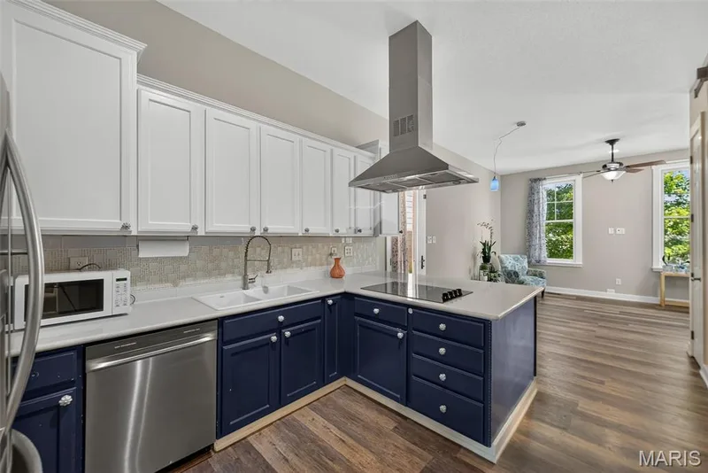 Modern kitchen featuring two-tone cabinetry, stainless steel appliances, a center island with cooktop, and wood-finish flooring — 3471 Hiram Street, St Charles, MO 63301