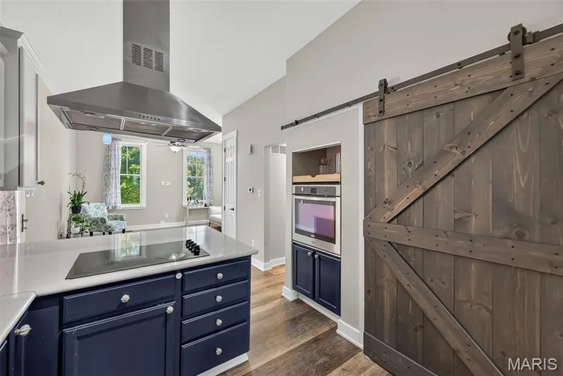 Contemporary kitchen featuring a navy blue island with multiple drawers and brushed nickel hardware, white subway tile backsplash, stainless steel range hood, and white cabinetry — 3471 Hiram Street, St Charles, MO 63301
