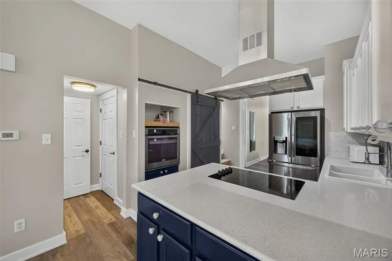 Chef's kitchen showcasing a large center island with quartz countertop, stainless steel range hood, and built-in stainless steel appliances including a dual-fuel range and refrigerator — 3471 Hiram Street, St Charles, MO 63301