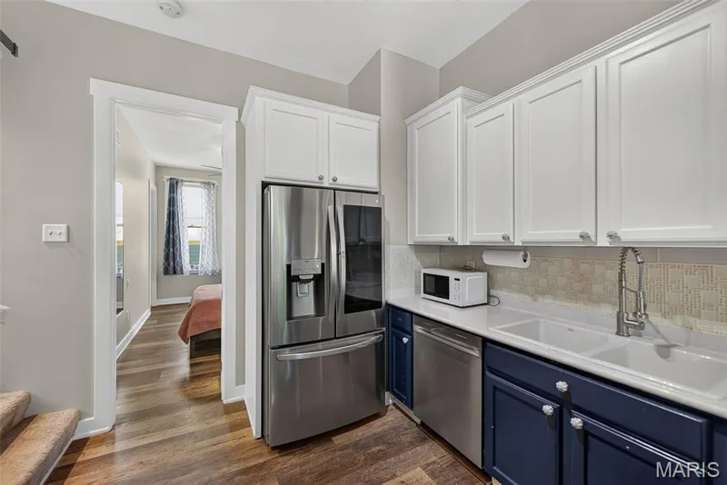 Modern kitchen featuring stainless steel French-door refrigerator with ice and water dispensers, white cabinetry with shaker-style doors, navy blue lower cabinets, quartz countertops, subway tile backsplash, stainless steel dishwasher, and a chrome pull-down kitchen faucet — 3471 Hiram Street, St Charles, MO 63301